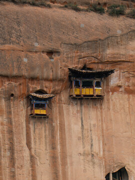View of ancient yellow and blue temples precariously cling to the rugged, striated red sandstone cliffs, defying gravity and time, Zhangye, Gansu, China.