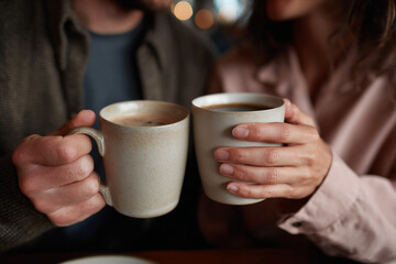 Man and woman clinking coffee mugs during breakfast.
