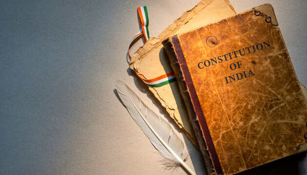 Top view of vintage Constitution of India book with feather quill pen and tricolor ribbon on old paper background for Republic Day history concepts