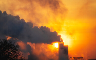 Silhouettes of industrial factories releasing smoke from their chimneys rise into the atmosphere, causing pollution at sunrise, environmental problems, air pollution