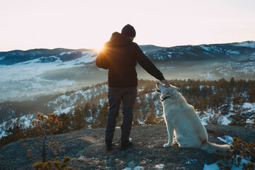 a man at a height in the mountains at sunset with a husky dog