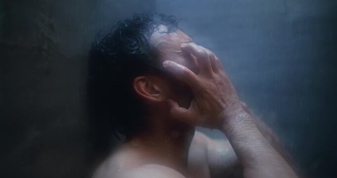 Man, shower and crying at glass with anxiety, stress and mental health with ptsd for sad memory. Person with depression, frustrated and grief with water drops for trauma in dark bathroom at apartment