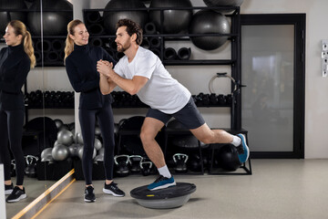 Man having a workout on a balance board, female coach helping him