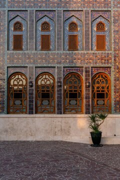 Doha, Qatar - 05 November 2025: View of intricate blue and beige mosaic patterns adorn a building's facade, punctuated by arched windows and doorways, glowing softly in the warm light.