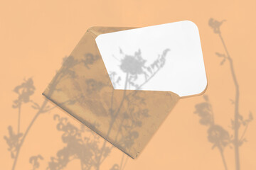 Natural lighting casts shadows from the wildflowers on an envelope with a sheet of white paper lying on a yellow background. Mockup