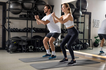 Two young people exercising in the gym in squatting position