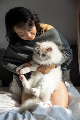 Woman Cradling Fluffy White Ragdoll Cat Like Baby on Bed Showing Adorable Pink Paw Pads