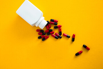 Medicine bottle spilling red and black capsules