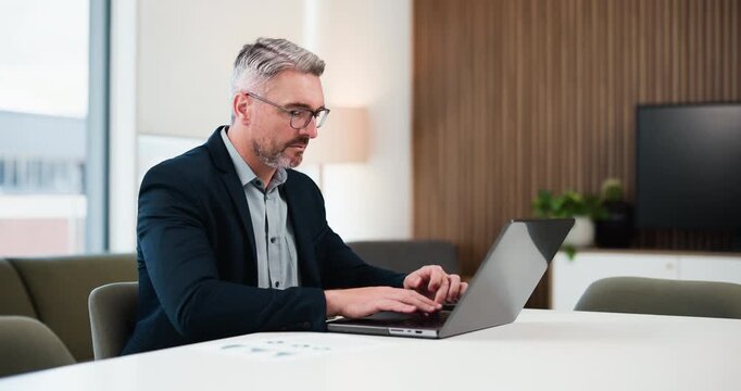 Businessman, smile and reading in office with laptop for data analysis, financial proposal or audit. Mature person, glasses or typing in workplace with computer, finance stats or accounting research.