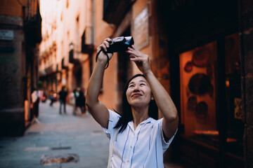 Smiling Asian tourist captures moment on digital camera, showcasing personal memory creation in tech age where visual storytelling supports identity and travel experience.