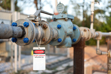 An isolation tag on oil production pipeline ball valve. This is lock out tag out safety sign to inform do not operate this equipment. Industrial safety sign object, close-up and selective focus.