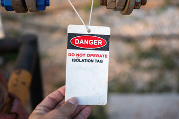 An isolation tag on oil production pipeline ball valve. This is lock out tag out safety sign to inform do not operate this equipment. Industrial safety sign object, close-up and selective focus.