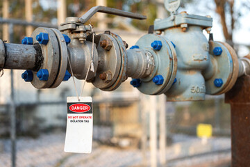 An isolation tag on oil production pipeline ball valve. This is lock out tag out safety sign to inform do not operate this equipment. Industrial safety sign object, close-up and selective focus.