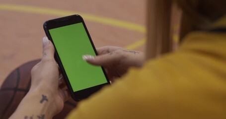Woman Holding Smartphone with Green Screen Chroma Key in Basketball Court Landscape View - Powered by Adobe