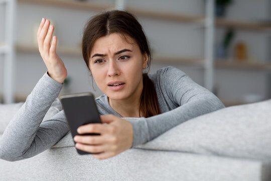 Angry sad shocked depressive attractive young caucasian female looking at phone and gesturing, got bad news at home interior, free space. Problems with device, wrong message and negative emotions