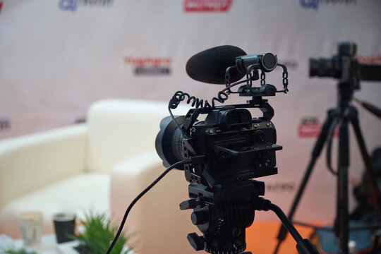 Small studio for recording interviews. Camera on a tripod in front of an empty chair and Press Wall.