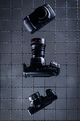 Three cameras are arranged on a gray tiled surface. The cameras vary in size and design, showcasing features like lenses and buttons. This setup is common for photography displays.