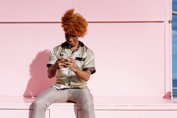 Young man with curly hair smiles while using smartphone, portraying connection, focus, and how mobile technology shapes communication in modern lifestyles