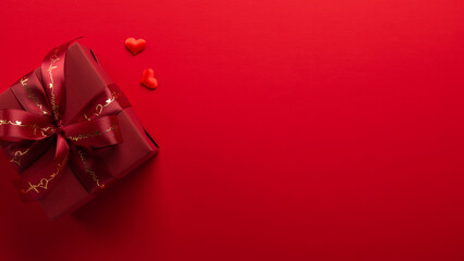 Gift, present box decorated with red ribbon bow, heart shape decoration on red background top view. Valentine's day, 14 February, birthday, 8 march women's day gift. Love and romance.