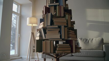 Creative christmas tree made of books with holiday decorations and gifts in living room