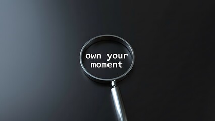 Fototapeta premium Magnifying glass focuses on white text 'own your moment' against a dark, reflective surface, symbolizing focus and seizing opportunities.