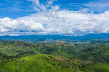 Expansive green hills and layered ridges stretch beneath a vivid blue sky filled with billowing clouds in the countryside between Phonsavan and Phou Khoun, Laos. The landscape features lush vegetation