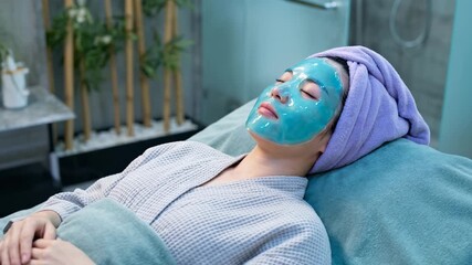 An Asian woman relaxing with a blue gel facial mask at a spa. A client receiving a professional skincare treatment in a beauty salon. Wellness and self-care concept