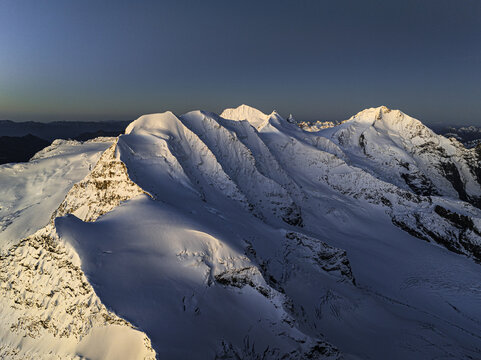 Aerial view of snow-covered peaks under a clear sky, a serene landscape of contrasting light and shadow, Piz Palu, Pontresina, Grisons, Switzerland.