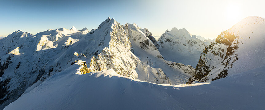 Aerial view of snow-capped peaks glisten under a radiant sun, casting long shadows across the pristine landscape, Piz Bernina Biancograt ridge, Pontresina, Grisons, Switzerland.