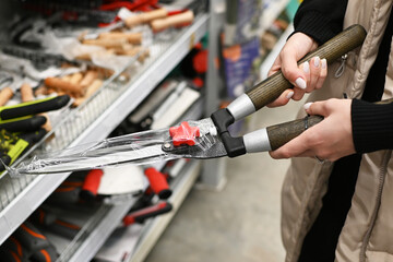Hands holding a pair of new garden shears in a hardware store aisle