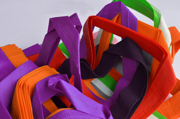 A collection of multicolored non-woven fabric tote bags. Textured and porous polypropylene straps.