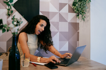 Freelancer reacts with wide smile and surprise while working, showing emotional impact of virtual communication and unexpected moments in digital freelance routine.