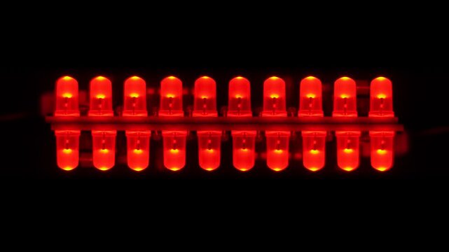 Two parallel rows of blinking bright red LED diodes glowing in the dark, close-up.