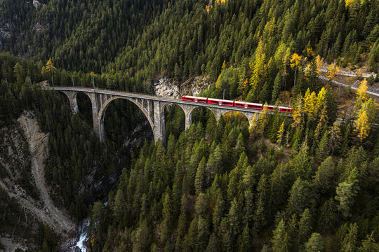 Aerial view of the Davos Wiesen Viaduct, a testament to engineering amidst a sea of green and gold autumn foliage, Davos, Grisons, Switzerland.