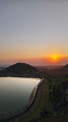 Obraz premium Serene sunset at a reservoir with a wooden bridge silhouette and calm water reflection at twilight.