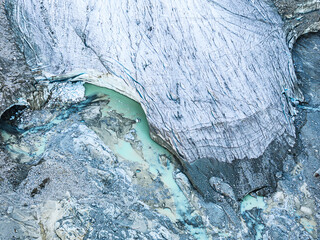 Aerial view of the stark, icy glacier scarred with deep crevasses and contrasted by a pool of turquoise meltwater, Morteratsch glacier, Pontresina, Grisons, Switzerland.