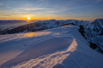 View of a snow-covered mountain range bathed in the warm glow of the setting sun, creating a stunning contrast with the cool blue sky, Nizna Bystra, Slovakia.