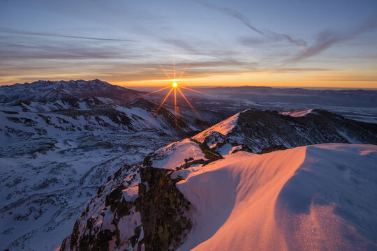 View of the sun cresting the horizon, painting the snow-capped peaks with golden light in the vast, icy wilderness, Nizna Bystra, Zilina region, Slovakia.