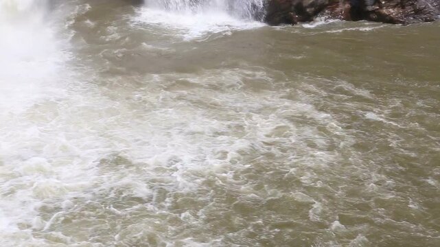 Powerful water flows from Maneri Dam on the Bhagirathi River, creating mist and strong currents across rocky terrain in the Himalayan region near Uttarkashi, Uttarakhand.
