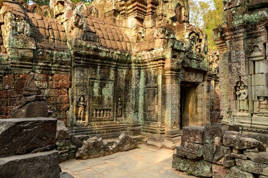 Ancient sandstone walls of Ta Som temple display intricate bas-reliefs and devata sculptures, illuminated by golden afternoon light in Cambodia's Angkor region. Weathered masonry and scattered stones