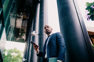 Confident African-American businessman in blue suit holding smartphone and tablet, looking aside with determination, symbolizing mobile leadership, connectivity and decision-making.