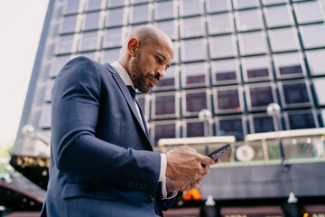 Low angle view of businessman sitting and concentrating on smartphone screen, conveying deep engagement, mobile productivity and modern digital independence in corporate routine.