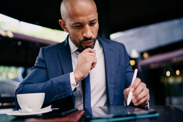 Focused businessman holding chin while using stylus on digital tablet, representing precision, planning and deep engagement with mobile tools in a smart tech-enabled business setup.