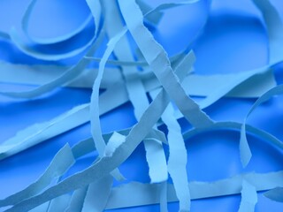 Crumpled and ripped light blue paper strips on blue background. Close-up.
