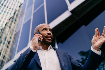 Smiling businessman gesturing mid-call with smartphone, showcasing clarity, confidence and seamless tech-enabled conversation in connected corporate lifestyle.