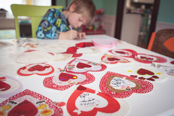 Young boy in pyjamas sitting at a table making heart shaped valentine cards