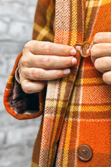  A woman buttoning her coat, vertical photo. A woman unbuttons her coat. women's fingers fastening a button. woman putting on coat. fingers fasten a button. autumn coat. Vertical photo