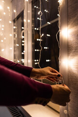 A woman connects a New Year's LED garland. LED garland on the window. preparation for the holiday. decorating a room with a garland. decorating a house with electric garlands. Vertical photo