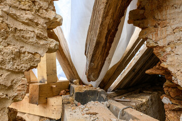 Aged wooden beams intersect within a rough stone wall, highlighted by raw textures and natural daylight filtering through a translucent tarp. The scene captures the craftsmanship and materials of