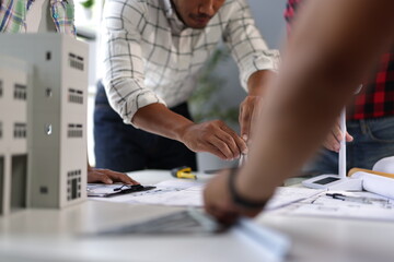 Engineers using compass on blueprint for new project with scale model and wind turbine.